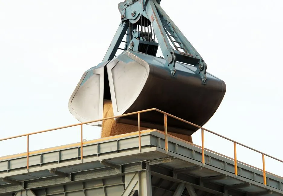 Clamshell grab unloading bulk cargo at an industrial port terminal.