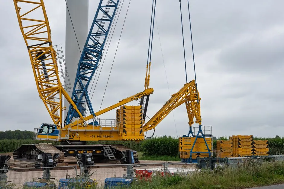Yellow construction crane lifting weights at an outdoor industrial site under cloudy skies.