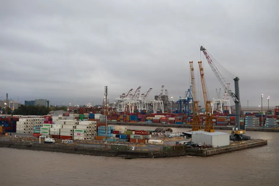 Expansive view of a busy industrial port with shipping containers and cranes under cloudy skies.